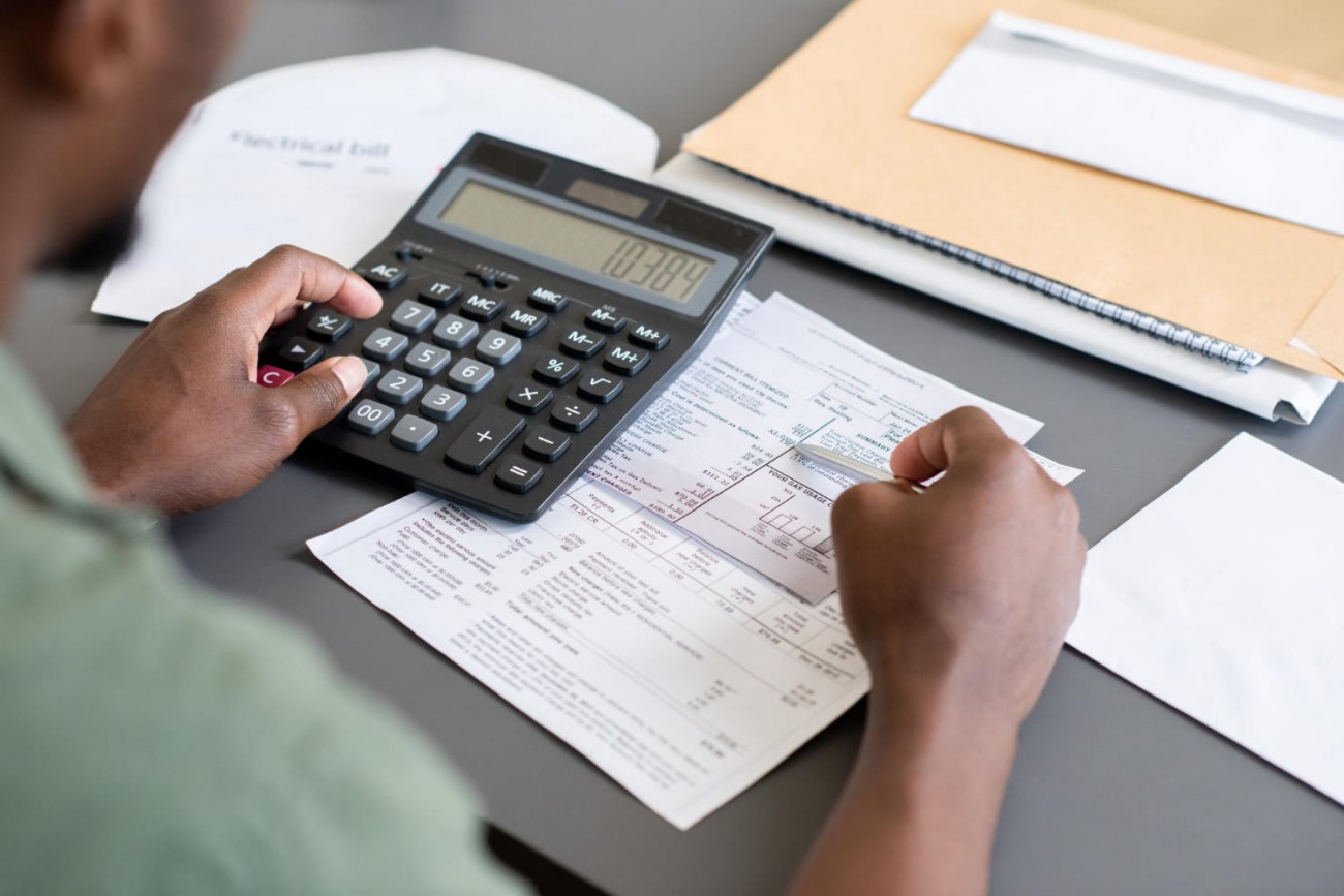 Pessoa com calculadora preta somando gastos no papel